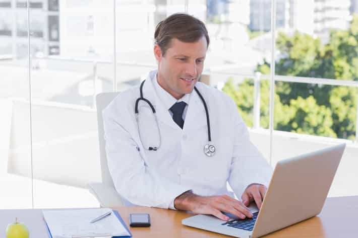 Happy doctor working on a laptop on his desk